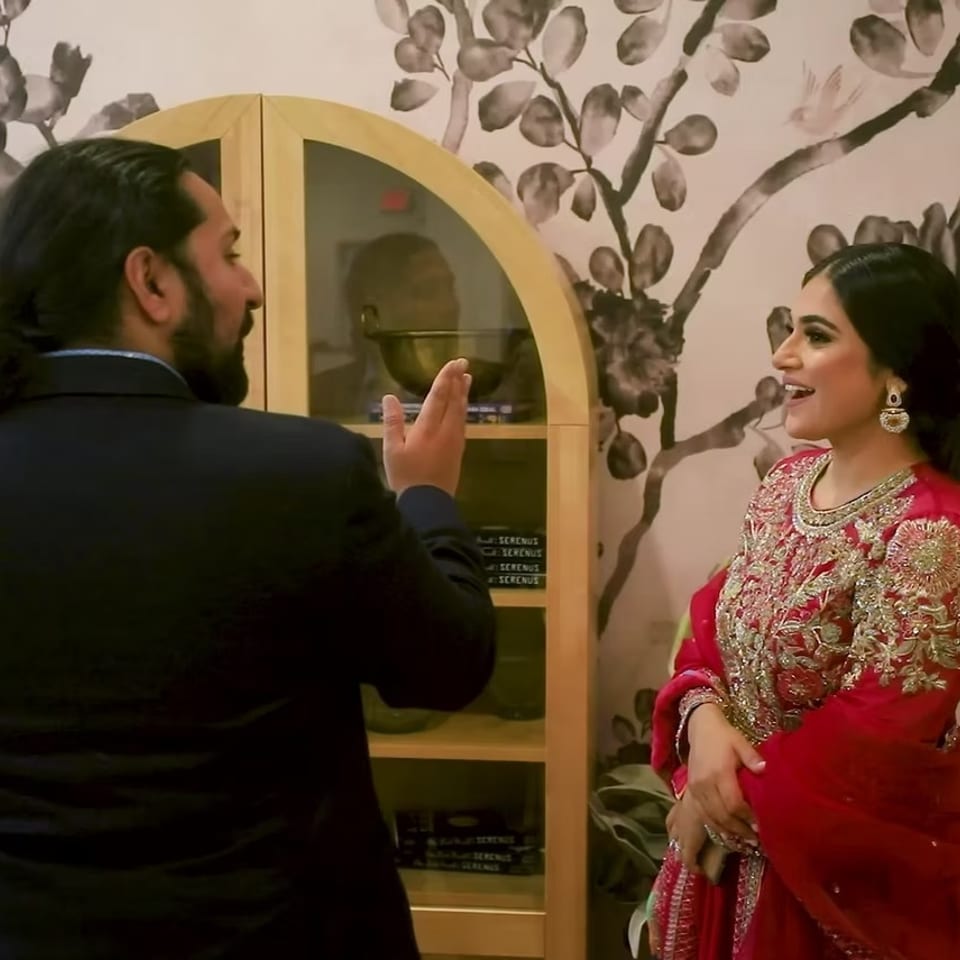 Man in a suit chats with a woman wearing an ornate red traditional outfit inside a floral-decorated restaurant.
