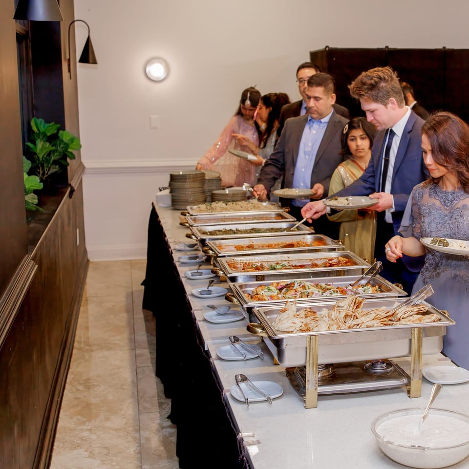 Guests serve themselves from a buffet of rice, vegetables, sauces, and flatbreads in an elegant dining room.