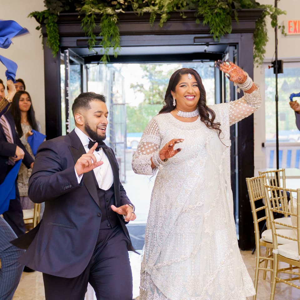 Bride and groom dance at a South Asian wedding reception as guests wave blue napkins around them.
